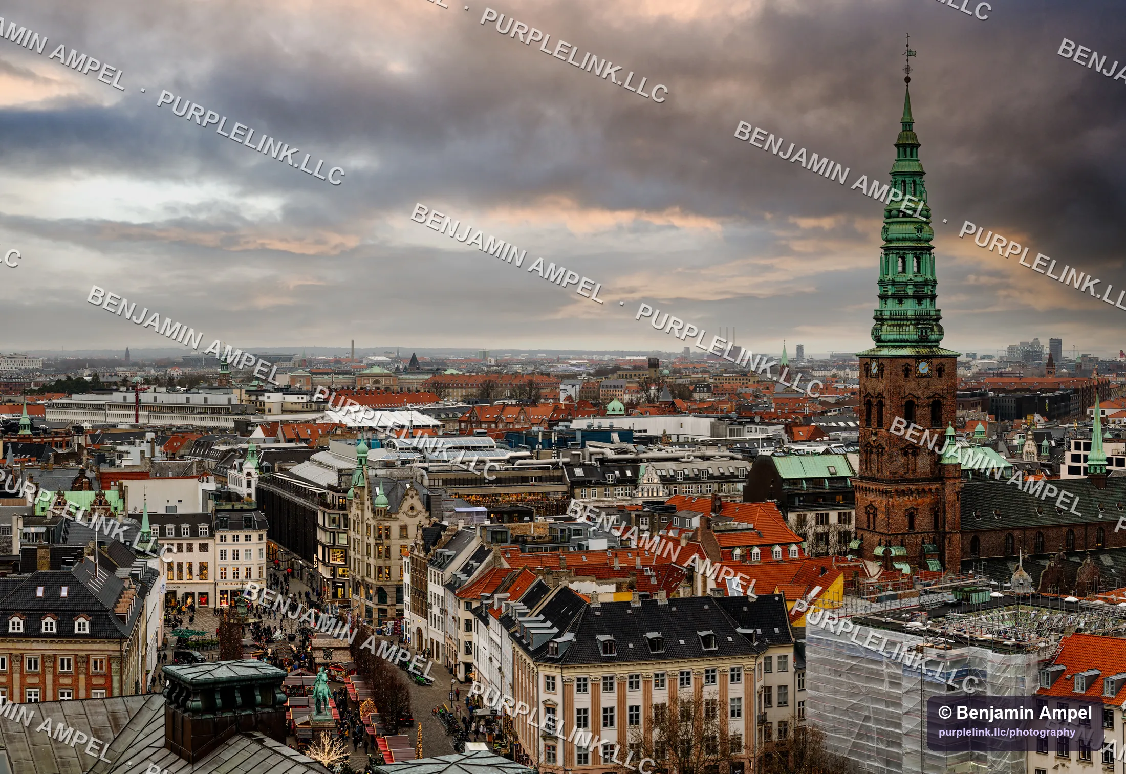 Copenhagen's red rooftops and a green copper spire under a broken, cloudy sky