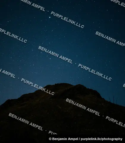 A clear night sky filled with stars stretches above the dark silhouette of a rounded desert mountain peak.