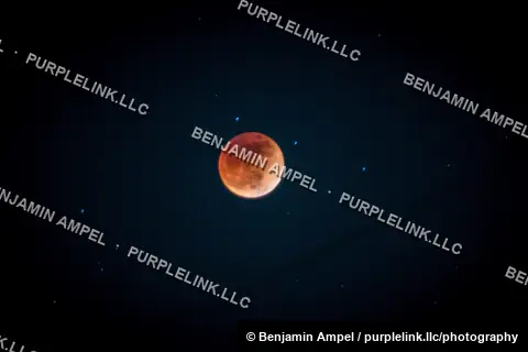 A deep orange-red blood moon glows during a total lunar eclipse, surrounded by faint stars in a dark night sky.