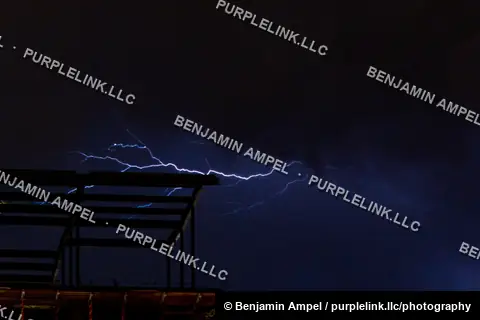 A bright lightning bolt streaks across a dark night sky above the steel framework of a building under construction.