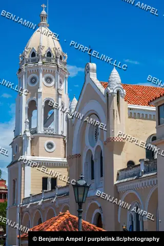 An ornate cream-colored colonial church with a domed bell tower and red tile roofs stands beneath a bright blue sky.