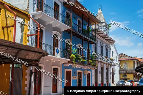 Casco Viejo, Panama City, Panama - August 2023: A restored blue and white colonial building with wrought iron balconies lines a sunny street, with a motorbike passing by.