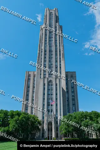 Pittsburgh, Pennsylvania - July 2022: The soaring Gothic tower of a university building rises above manicured lawns and trees under a clear blue sky.