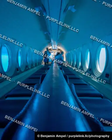 Waikiki, Hawaii - January 2024: The long, blue-lit passenger cabin of a tourist submarine stretches into the distance, lined with round portholes and rows of seating.