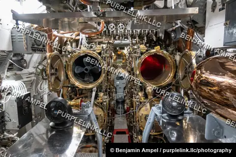 The polished brass torpedo tubes and pipework of a WWII-era submarine's forward torpedo room, preserved as a museum exhibit.