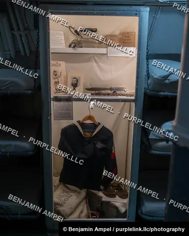 Pearl Harbor, Hawaii - January 2024: A glass display case aboard a historic submarine shows a sailor's uniform, personal photograph, and wartime belongings.