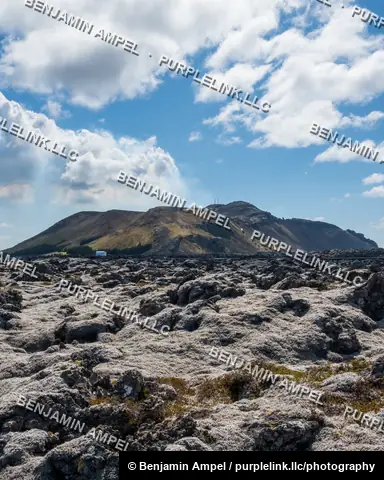 Iceland - June 2024: A vast field of moss-covered lava rock stretches toward a flat-topped mountain under a partly cloudy sky.