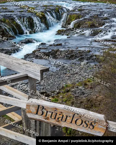 Iceland - June 2024: A carved wooden sign reading Bruarfoss marks a footbridge railing overlooking the vivid blue waterfall below.