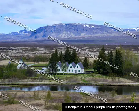 Iceland - June 2024: A layered volcanic mountain ridge with patches of snow rises above green highland fields under a partly cloudy blue sky.