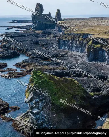 Lóndrangar, Snæfellsnes, Iceland: twin volcanic sea stacks rise beside layered basalt cliffs dotted with nesting seabirds above the Atlantic.