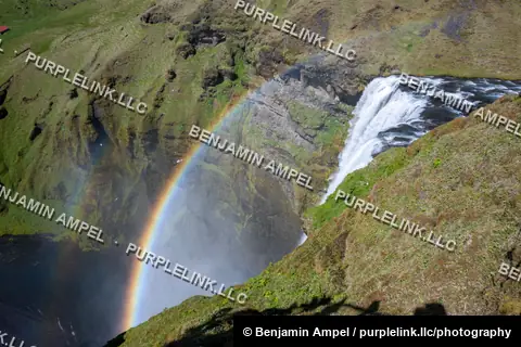 A double rainbow spans the canyon beside Skógafoss waterfall, viewed from an elevated vantage point in south Iceland.