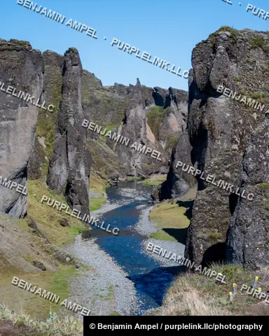 Fjaðrárgljúfur canyon's layered rock spires rise above a winding river cutting through the mossy gorge, south Iceland.