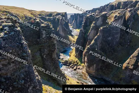 A wide view over Fjaðrárgljúfur canyon shows its layered rock walls winding toward the distant Icelandic coastline.
