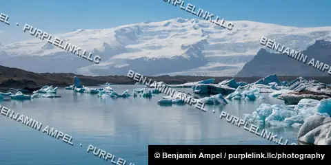 A wide panorama of Jökulsárlón glacier lagoon shows scattered icebergs beneath the snow-covered Vatnajökull ice cap, Iceland.
