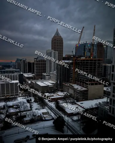 Atlanta, Georgia - January 2025: The downtown skyline glows at dusk after a snowfall, with construction cranes and illuminated signage among the high-rise buildings.