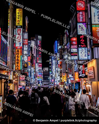 Tokyo, Japan - June 2025: Crowds of pedestrians walk down a neon lit Kabukicho street in Shinjuku lined with bars, restaurants, and illuminated signage.