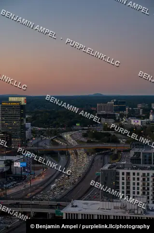 An aerial view of Atlanta, Georgia shows a busy interstate highway with streaking traffic lights winding through downtown skyscrapers at dusk.