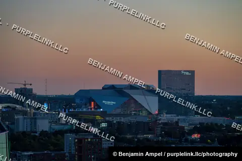 An aerial view of downtown Atlanta, Georgia at dusk shows illuminated corporate office towers against a warm orange horizon.