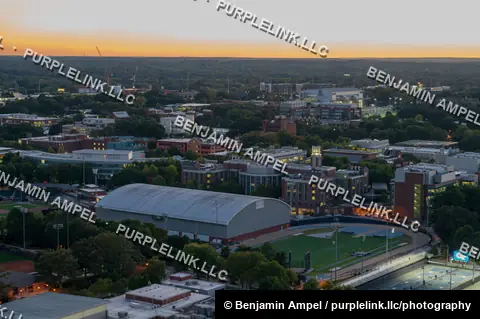 An aerial view of the Georgia Tech campus in Atlanta at dusk shows athletic facilities, tennis courts, and academic buildings with the city skyline beyond.