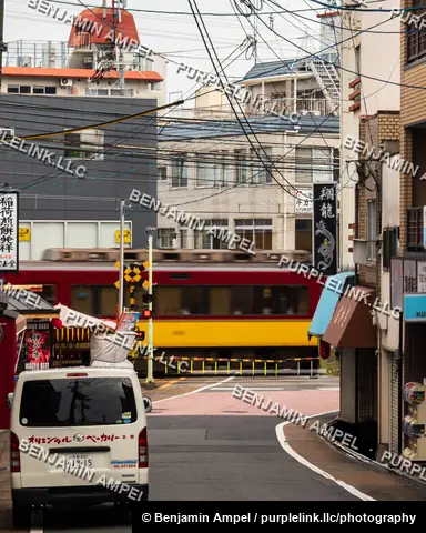 Fushimi Inari, Kyoto - a white delivery van waits as a red and yellow train crosses the street beneath a tangle of power lines near shop signage advertising wagyu beef.