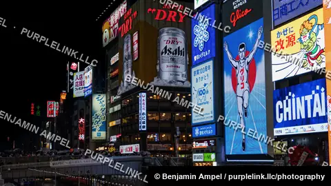 Brightly lit billboards including the iconic Glico running man sign and Asahi beer advertisement glow above the Dotonbori canal in Osaka, Japan.