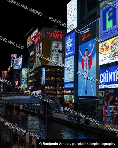 Neon billboards including the iconic Glico running man sign glow above the Dotonbori canal as boats pass below in Osaka, Japan.