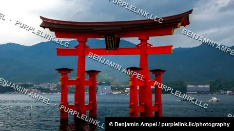 The iconic red torii gate of Itsukushima Shrine stands in the sea with forested mountains in the background.