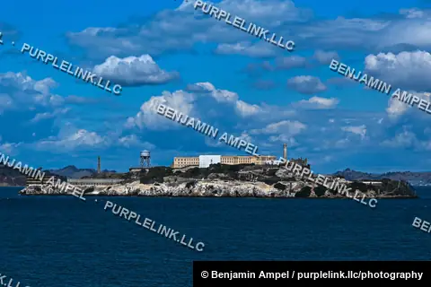 The former Alcatraz prison sits on its rocky island in San Francisco Bay beneath a sky filled with puffy clouds.