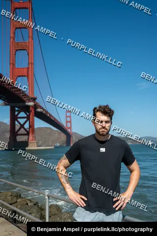 A man wearing a Nike t-shirt stands with hands on hips in front of the Golden Gate Bridge and San Francisco Bay.