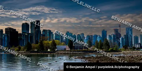 Vancouver's downtown skyline rises beyond a rocky low-tide shoreline and a historic red brick building near Stanley Park.