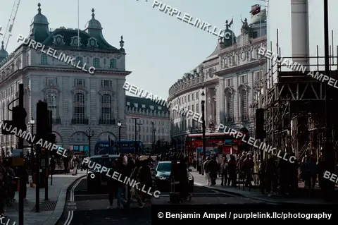 London, England - October 2025: Traffic and pedestrians pass historic curved buildings near Piccadilly Circus with a red double-decker bus and construction scaffolding.