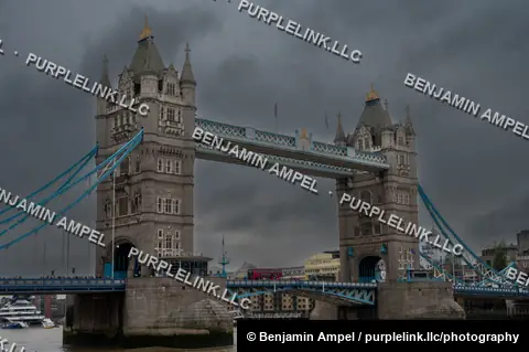 The twin towers of Tower Bridge span the River Thames beneath dark storm clouds in London.