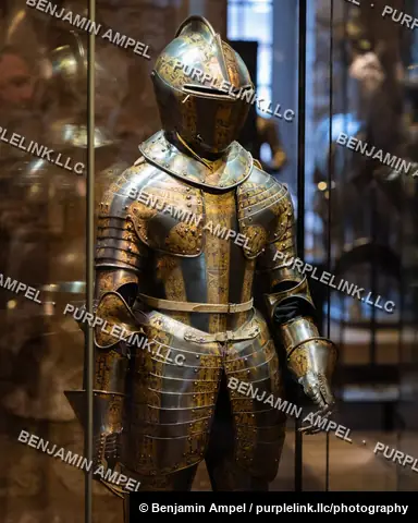 London, England - October 2025: An etched and gilded suit of plate armor with a visored helmet is displayed behind glass at a London museum.