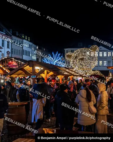 Copenhagen, Denmark - December 2025: Strollers walk along a rain-slicked pedestrian shopping street strung with oversized red heart lights and holiday garlands at night.