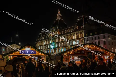 Copenhagen, Denmark - December 2025: Illuminated wooden Christmas market stalls stand before the domed Magasin du Nord department store at night.