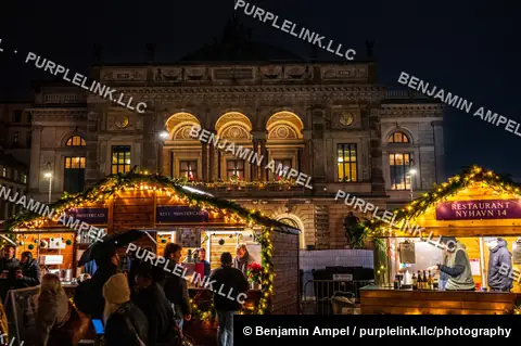 Copenhagen, Denmark - December 2025: Wooden holiday market stalls trimmed with lights stand in front of the illuminated Royal Danish Theatre building at night.