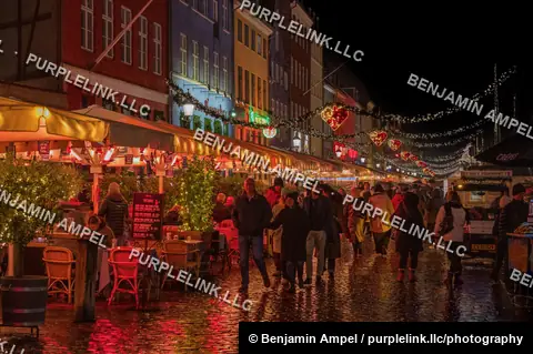 Copenhagen, Denmark - December 2025: Pedestrians walk along the Nyhavn waterfront strung with red heart-shaped lights and holiday garlands above outdoor cafe seating.