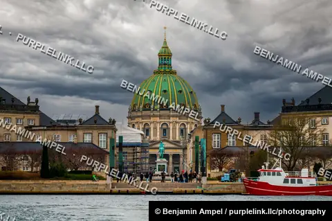 Copenhagen, Denmark - December 2025: The green copper dome of Frederik's Church (Marmorkirken) rises above Amalienborg's colonnades under a dramatic, storm-lit sky, with a red fishing boat moored in the foreground harbor.