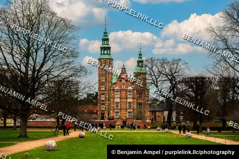 Copenhagen, Denmark - December 2025: Rosenborg Castle's twin spires rise beyond a formal garden lined with bare trees and sculpted topiary spheres under a partly cloudy sky.