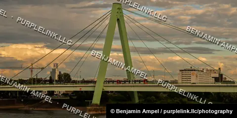 A commuter train crosses the cable-stayed Severins Bridge over the Rhine river in Cologne at dusk.