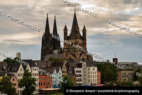 Gothic cathedral spires and the Great St. Martin church tower over Cologne's colorful old town houses along the Rhine at dusk.