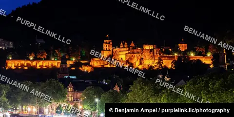 The red sandstone ruins of Heidelberg Castle glow under floodlights against a dark forested hillside at night.