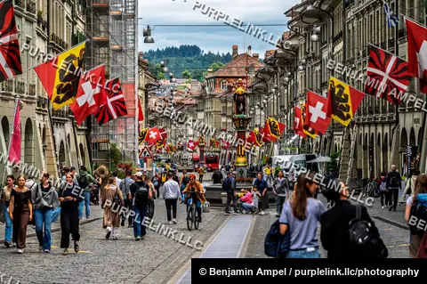 Bern, Switzerland - June 2026: Pedestrians walk beneath rows of Swiss and cantonal flags on a bustling street in Bern's old town.