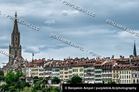 The Gothic spire of Bern Minster rises above the red rooftops of Bern's historic old town under a cloudy sky.