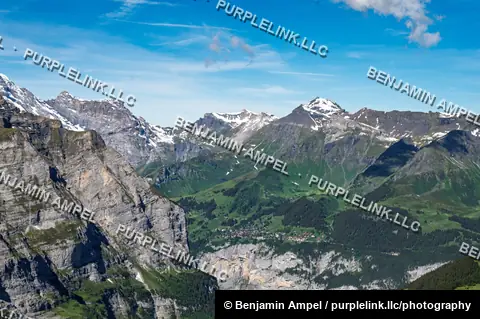 Rugged snow-dusted mountain ridges surround a small alpine valley village seen from high above in the Swiss Alps.