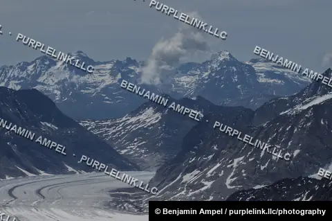 The Aletsch Glacier winds between rugged snow-covered mountain ridges beneath a hazy sky in the Swiss Alps.