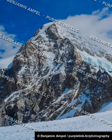 A jagged snow-covered mountain summit rises sharply against a deep blue sky in the Swiss Alps.