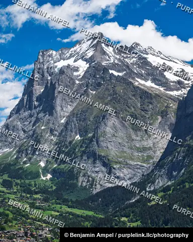 The rugged, snow-streaked Wetterhorn peak towers above the green valley and village of Grindelwald in the Swiss Alps.