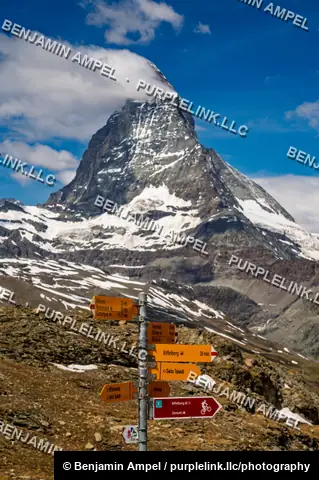 Zermatt, Switzerland - June 2026: A wooden trail signpost with directions to Riffelberg and Zermatt stands before the towering Matterhorn peak.