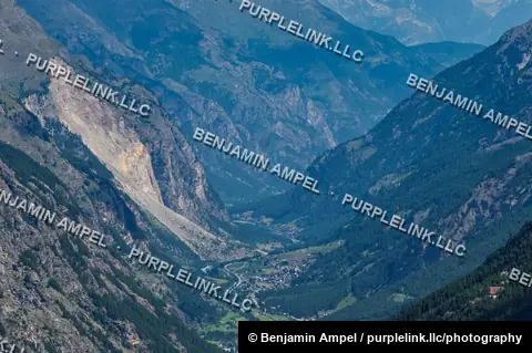 A deep forested valley with a small alpine village winds between steep mountain slopes near Zermatt.